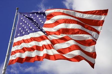 Flag flying against a blue sky with fluffy clouds.